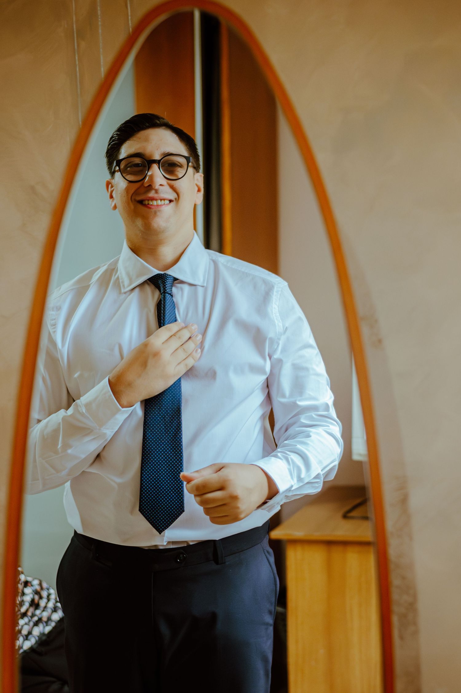 A person in formal attire adjusting a navy blue tie while getting ready.