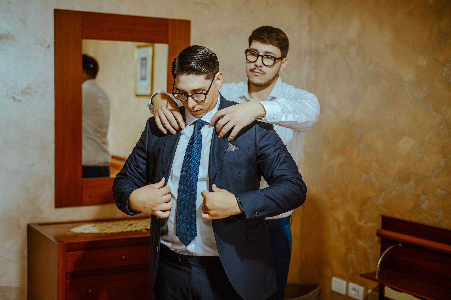 Two people in formal wear helping each other prepare for an event.