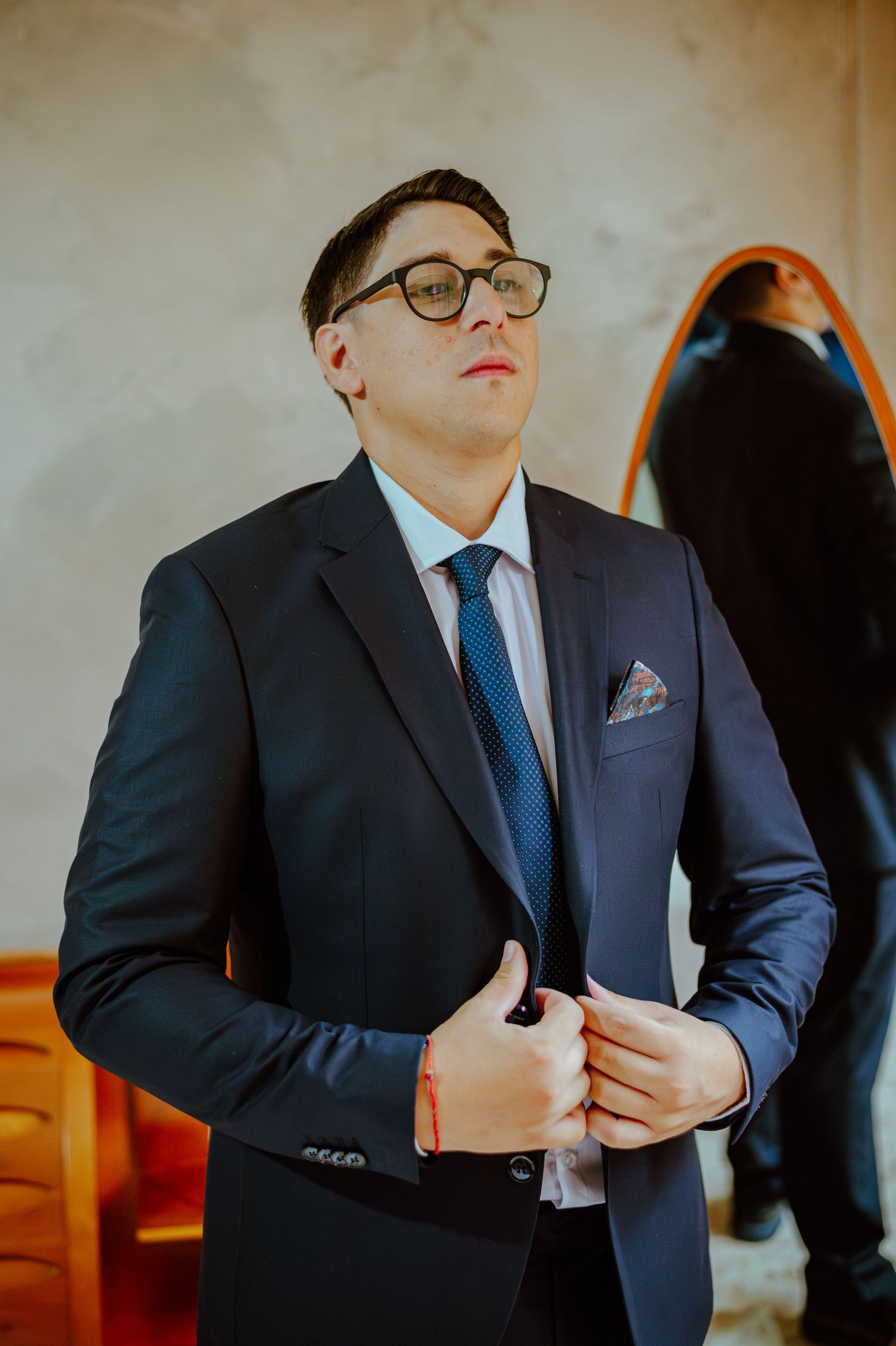 A person wearing glasses and navy suit with pocket square preparing for formal occasion.