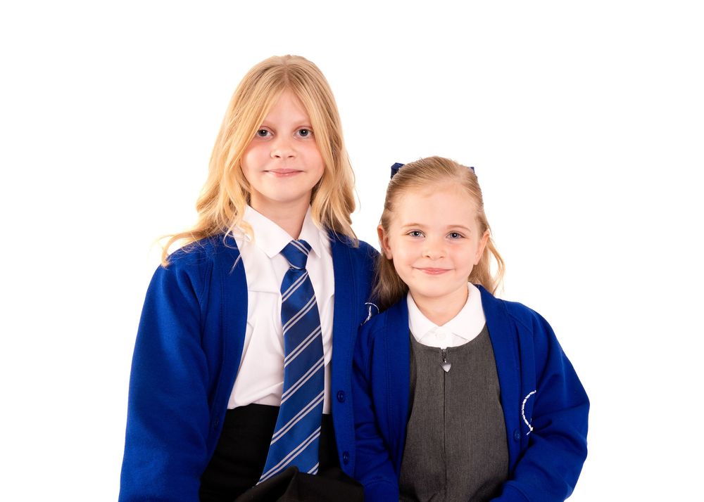 Two young girls in blue school uniforms and ties posing together against a white background.