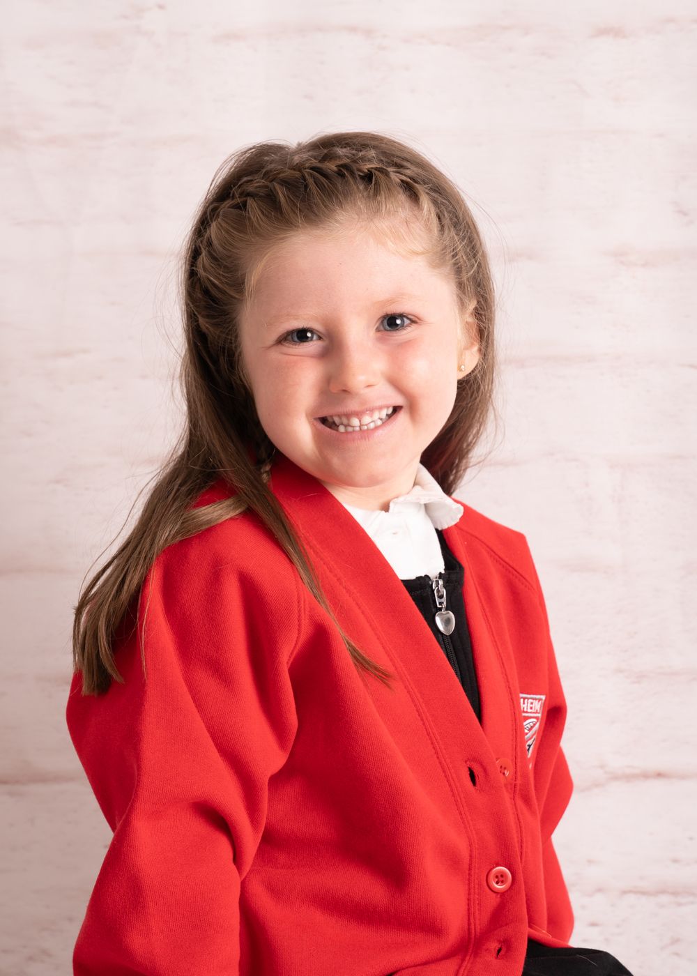 A child in a bright red cardigan smiles while posing against a white background.