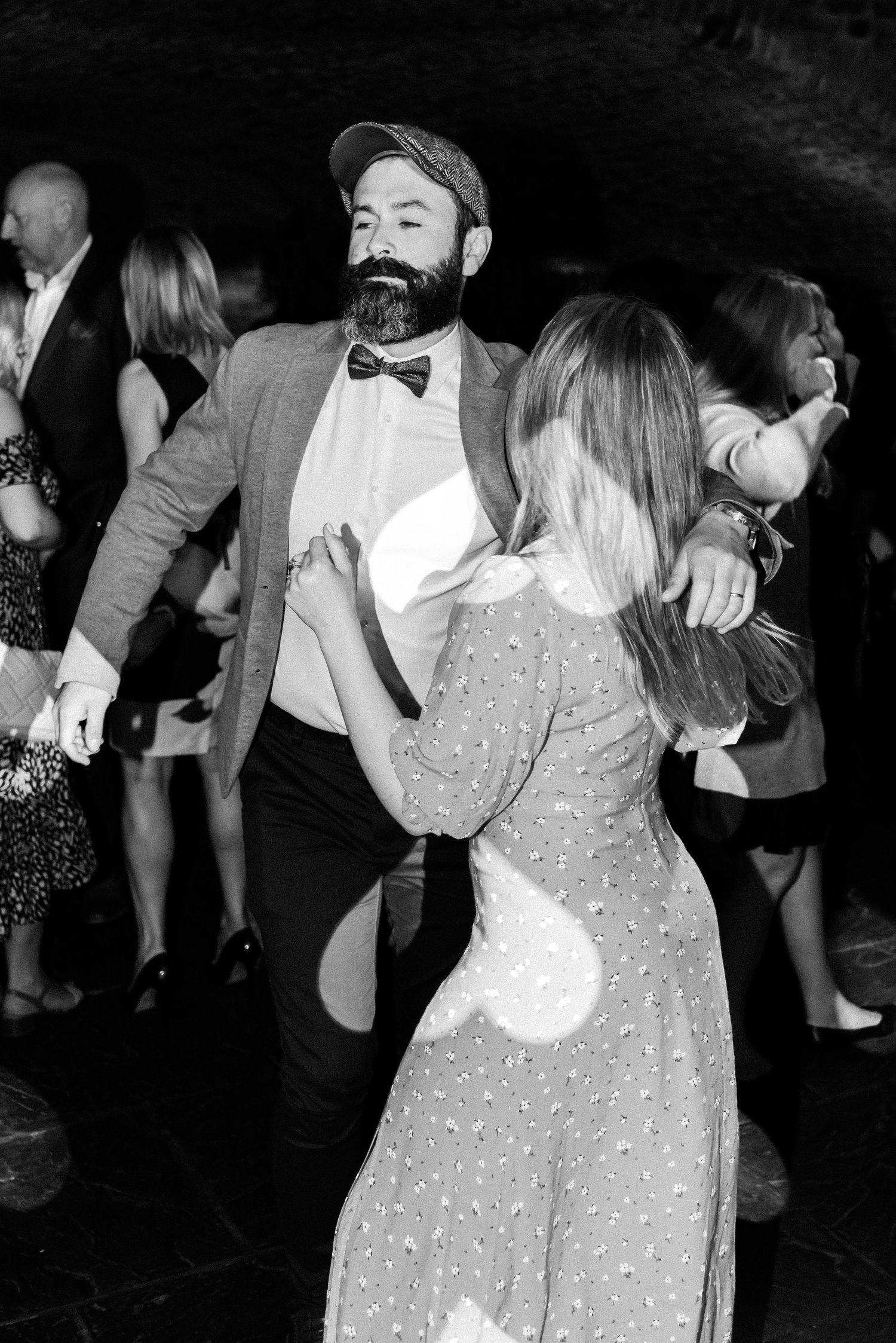 A couple dances together at a formal event, with the man wearing a bow tie and the woman in a sparkly dress.