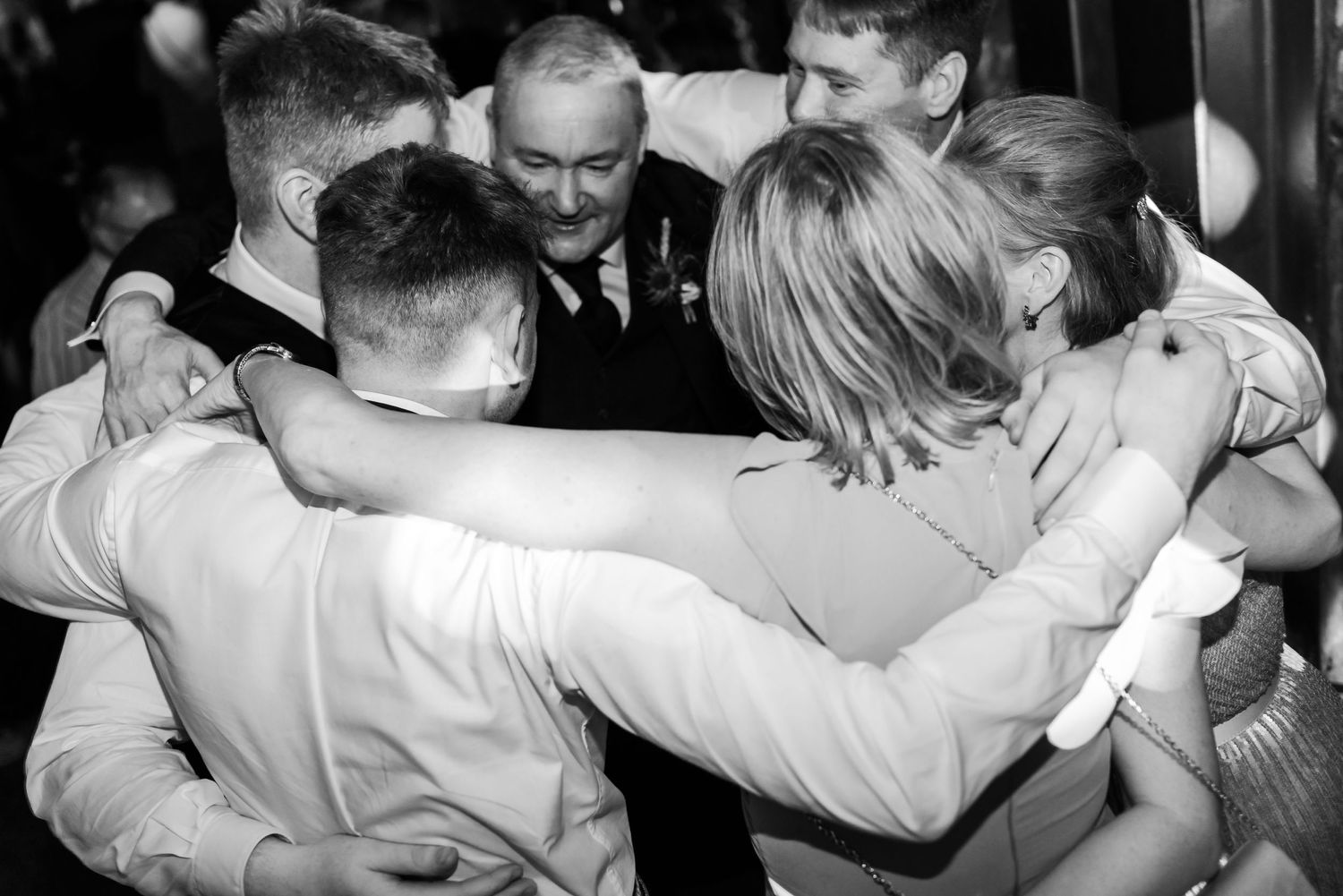A group of guests embrace in a warm group hug during an emotional celebration moment.