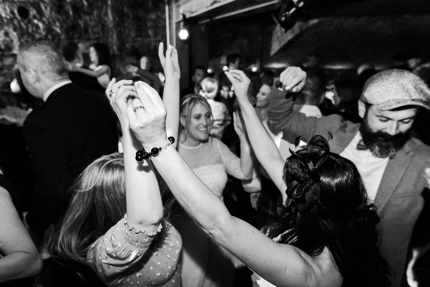 Party guests raise their hands in celebration while dancing under venue lighting.