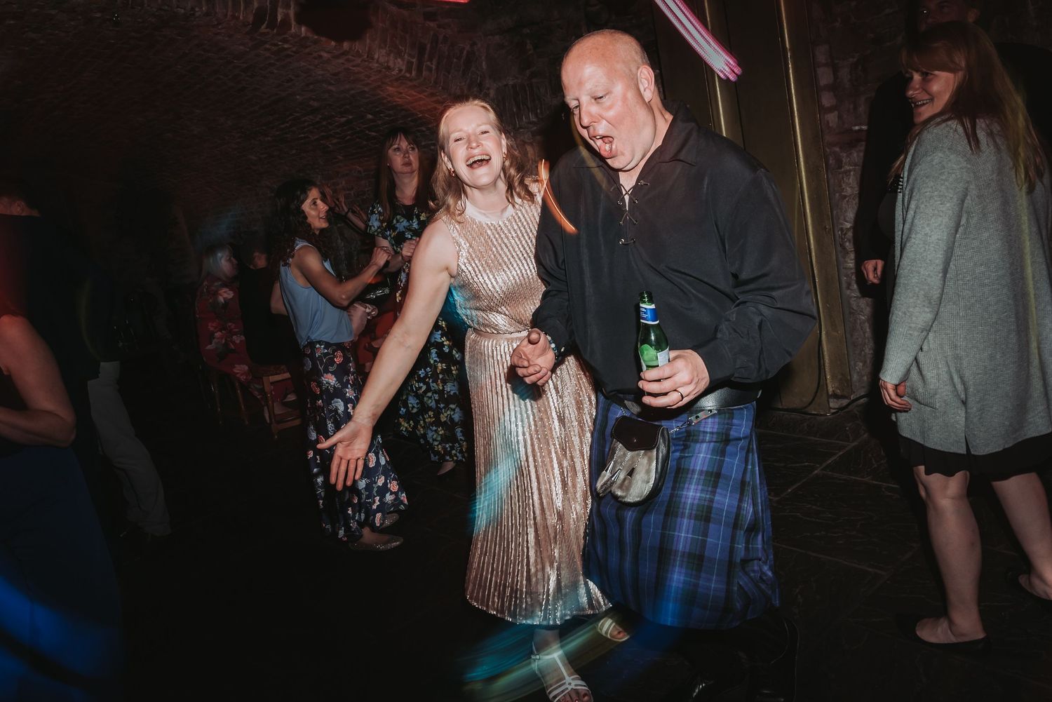 Partygoer in a kilt dances enthusiastically in a dimly lit venue.