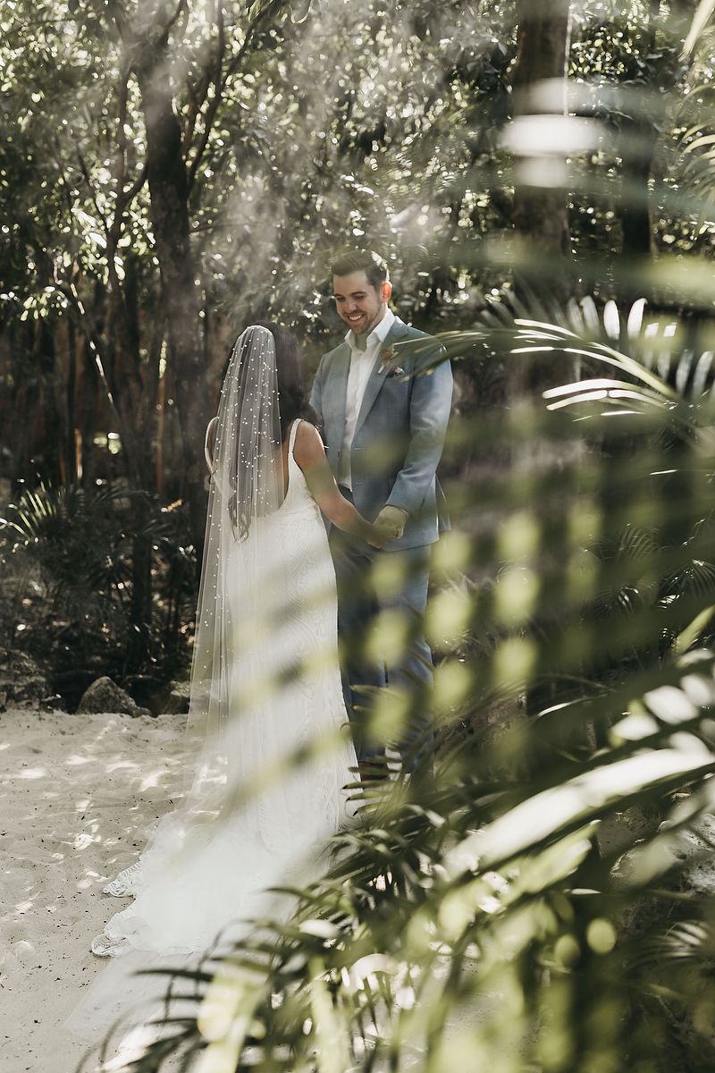 Bride and groom share a romantic first look moment surrounded by lush tropical greenery in a forest setting.