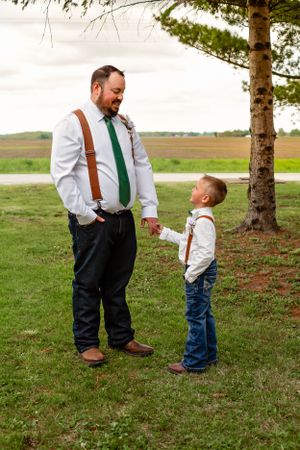 Sweet candid moment between groomsman and young ring bearer outdoors.