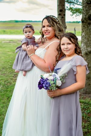 Wedding party members in purple dresses pose together outdoors.