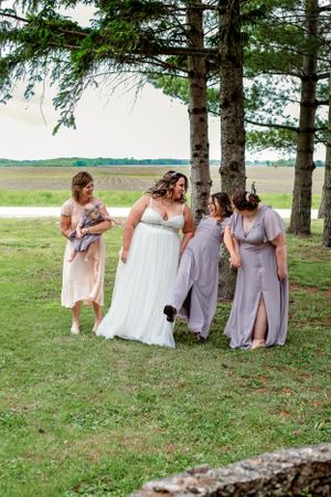 Bridal party in pastel dresses walking together on grassy lawn.