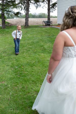 Wedding photo showing dress detail with ring bearer in background.