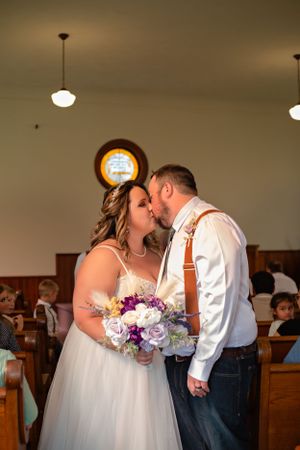A romantic wedding moment captured in a church with soft lighting and a beautiful bouquet of purple flowers.