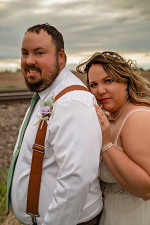 Close-up wedding portrait of a couple in casual attire with rustic background.