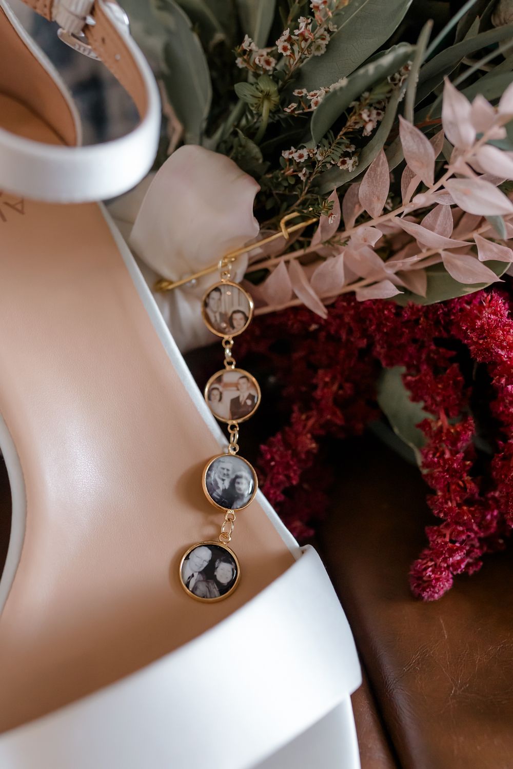 Elegant white bridal shoe with decorative charm detail next to burgundy and pink florals.