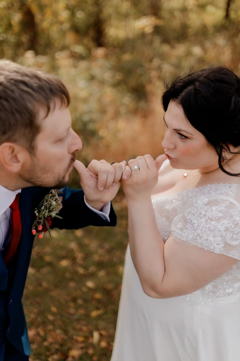Romantic wedding couple sharing a playful pinky promise moment in autumn woods.