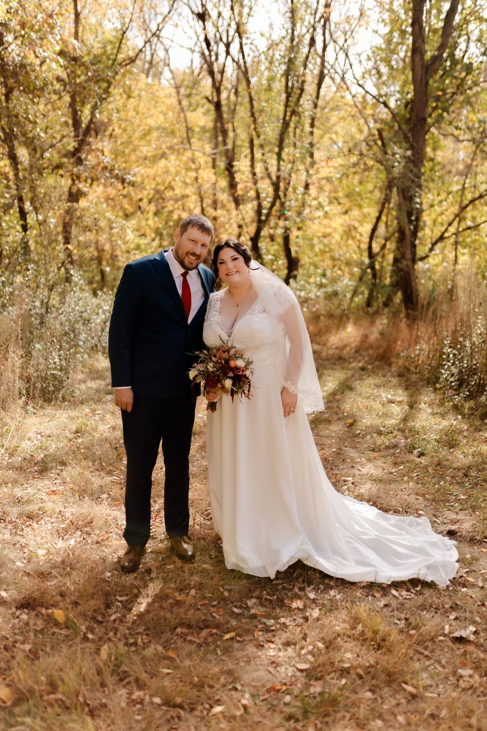 Autumn wedding portrait with golden leaves and trees in background.