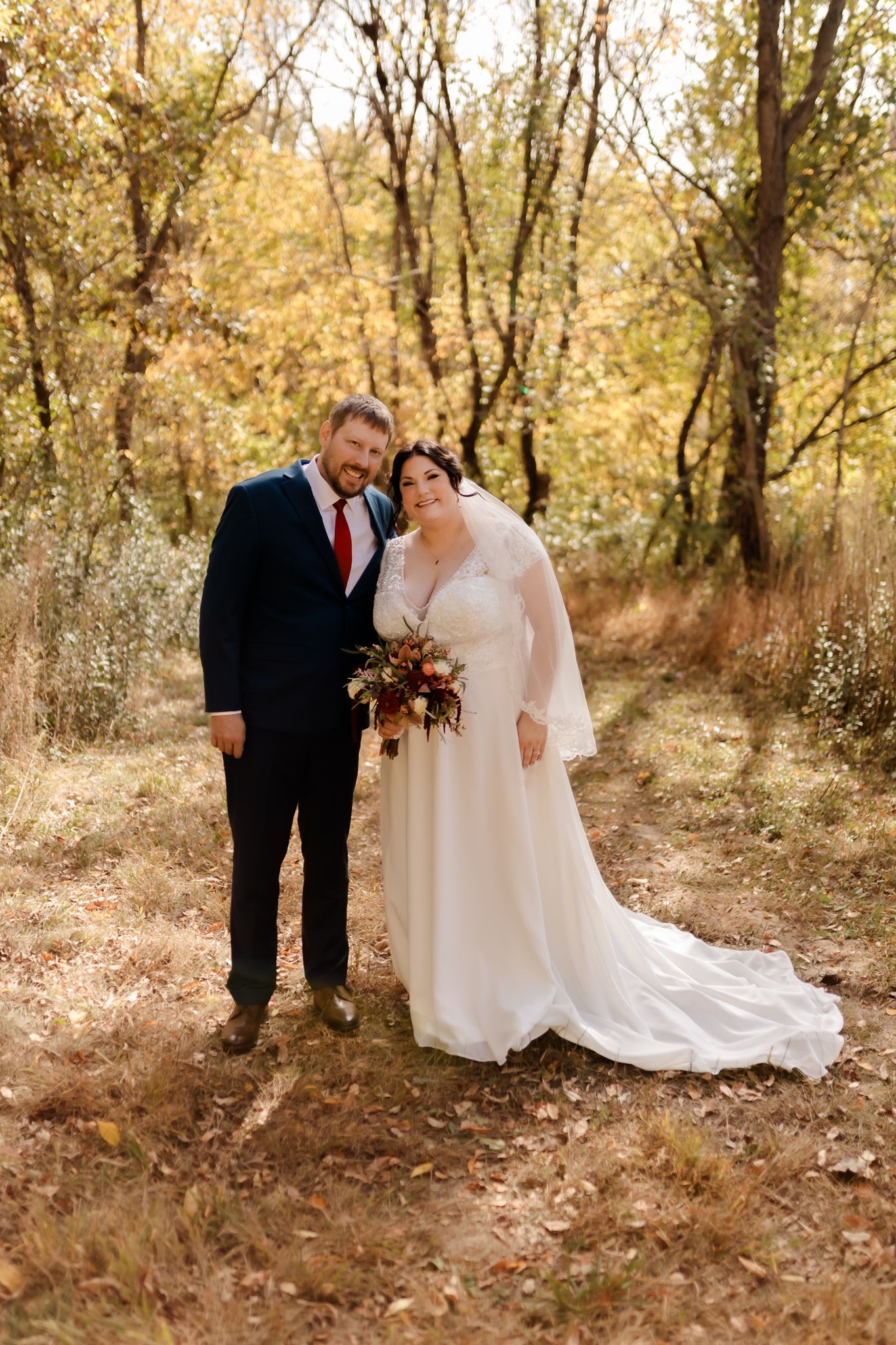 Autumn wedding portrait with golden leaves and trees in background.