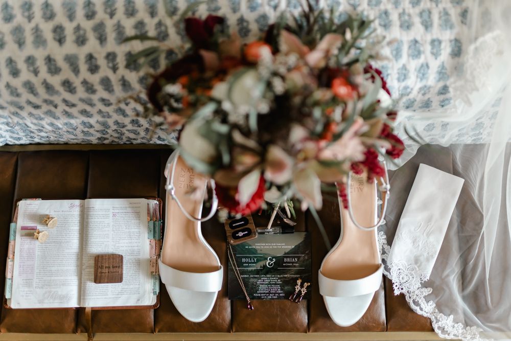 Wedding accessories including white bridal shoes, floral bouquet and lace veil arranged on wooden surface.