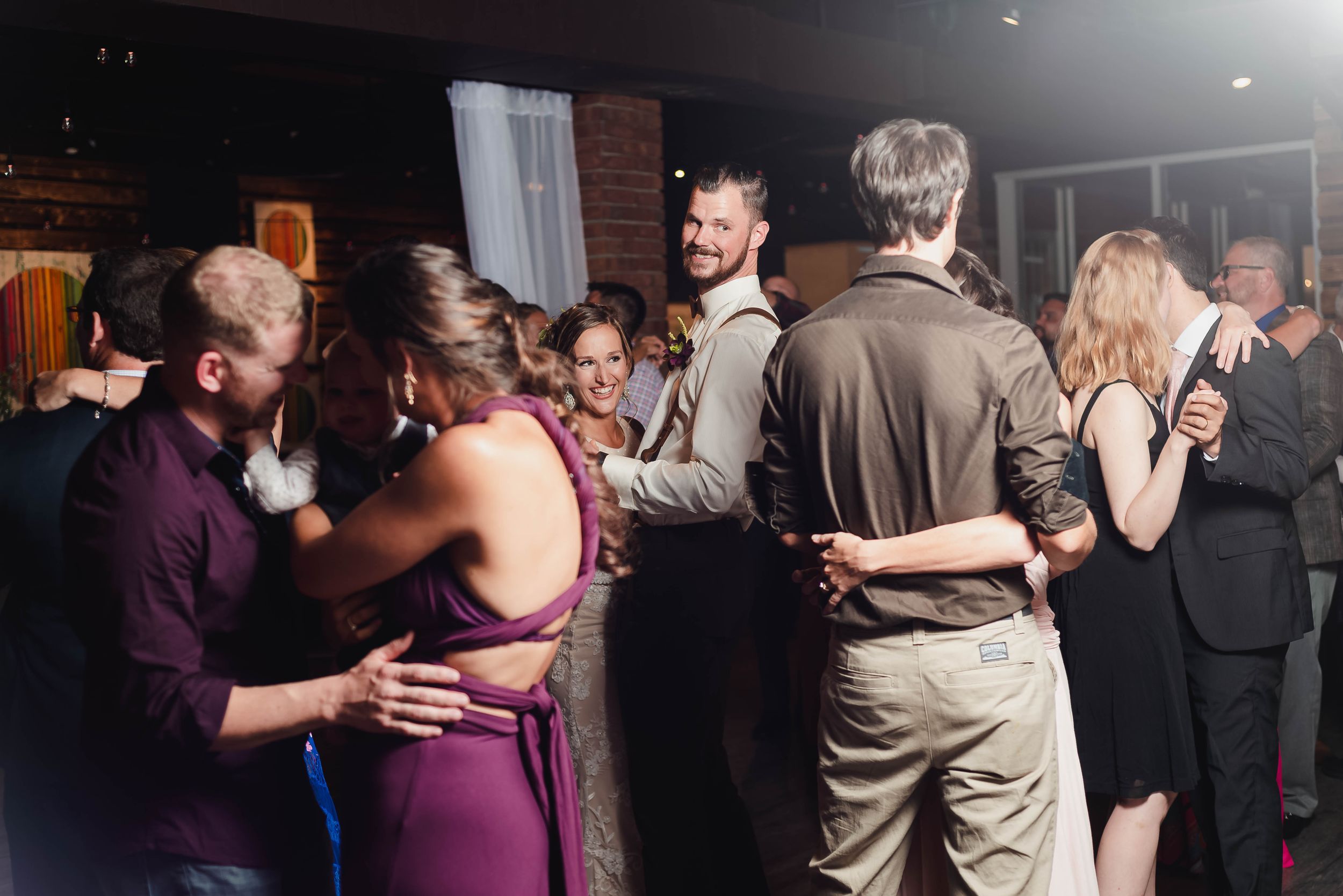 Wedding guests dancing and celebrating together at a dimly lit reception venue.