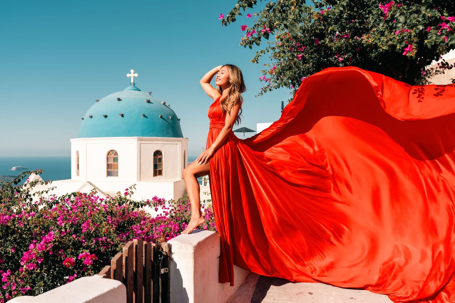 Person in flowing orange dress poses dramatically overlooking Mediterranean sea view.