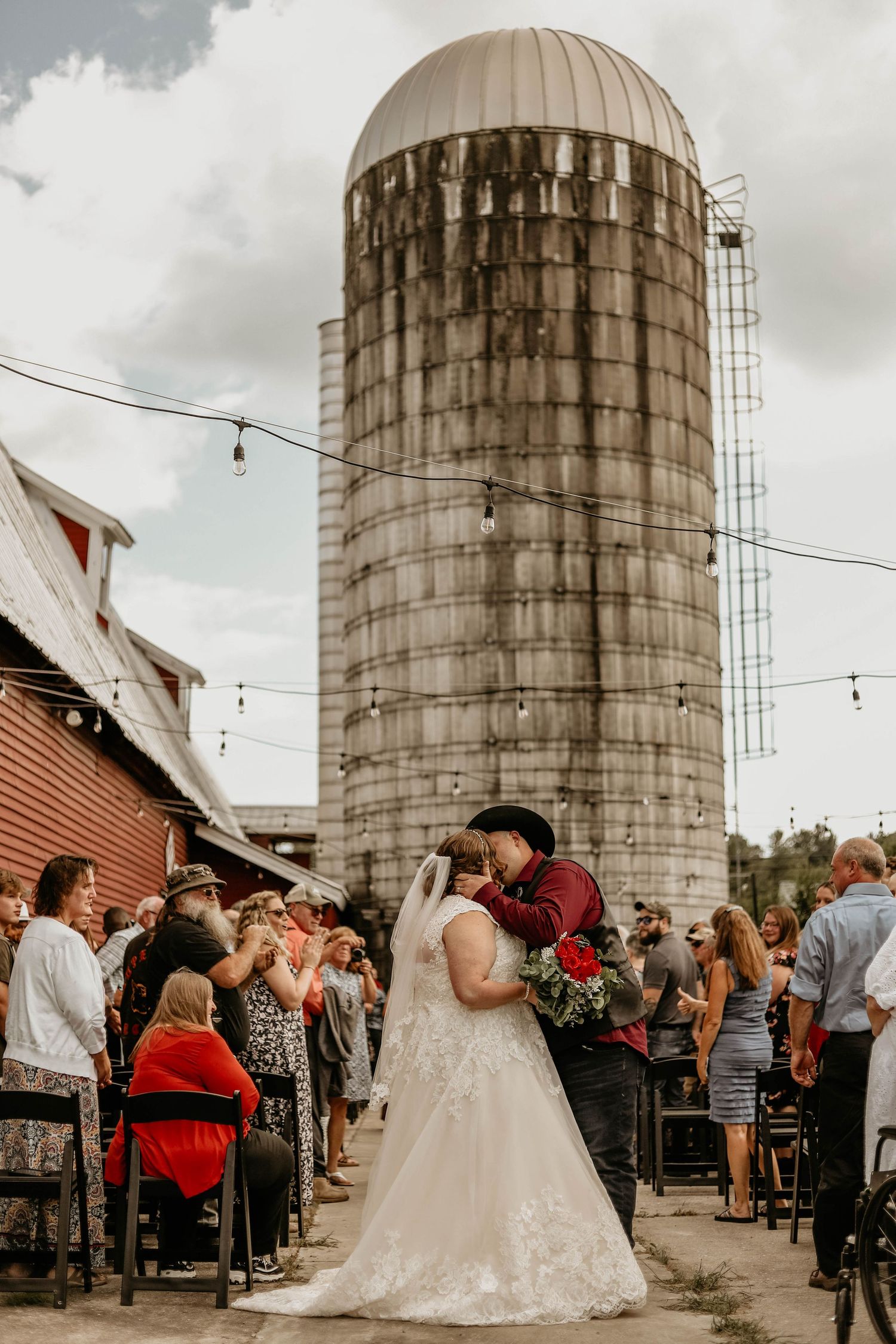 A wedding celebration at a rustic farm venue with a large silo in the background.