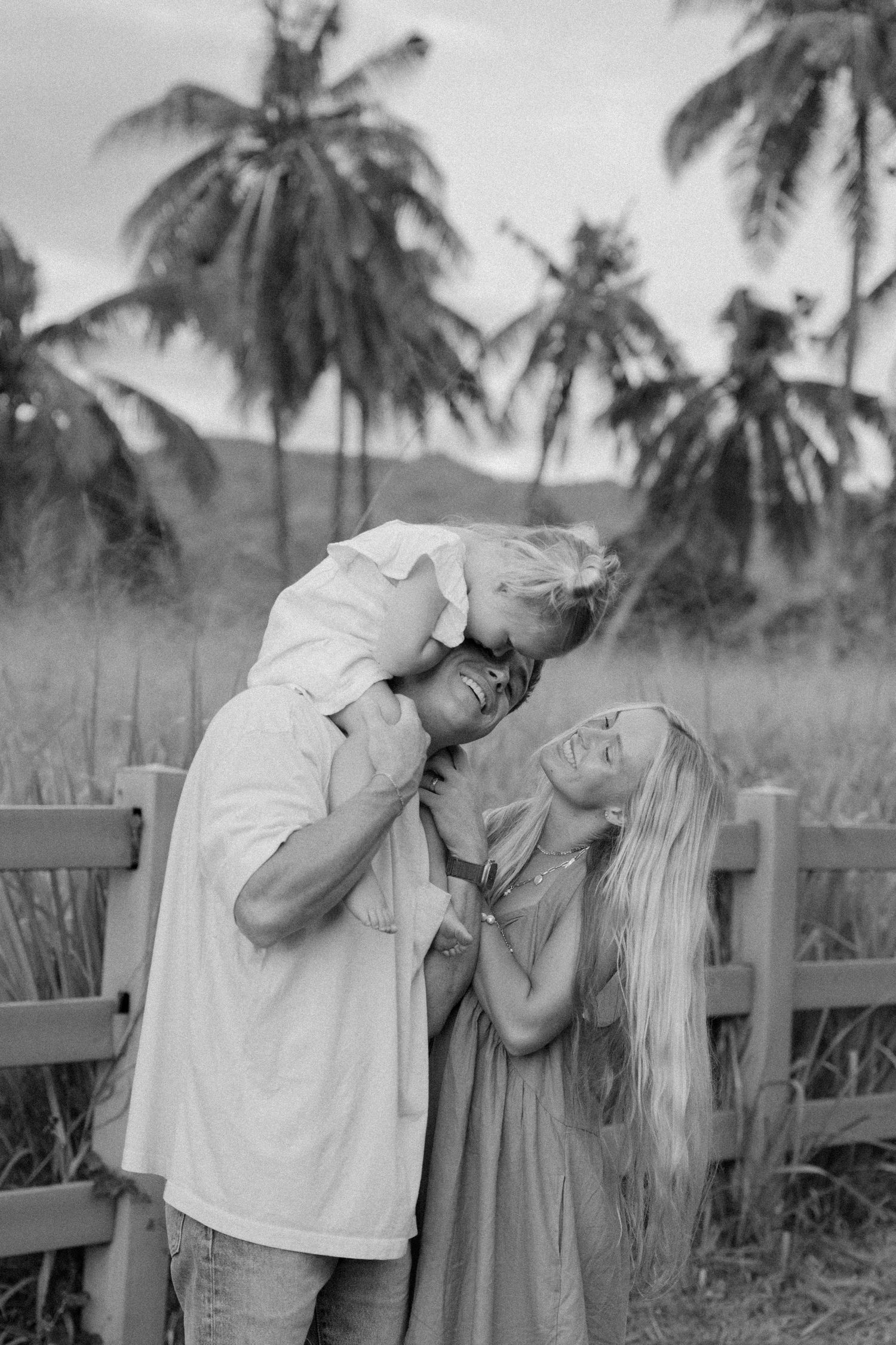 A joyful family moment captured against palm trees in black and white.