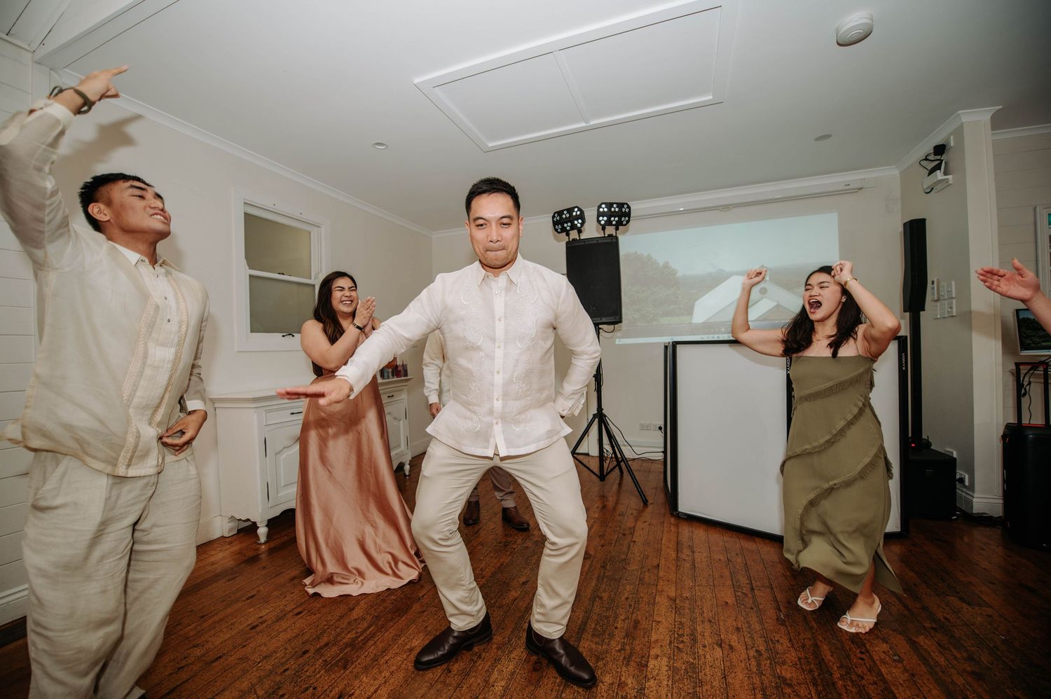 Wedding party members dancing energetically on wooden floor during reception celebrations.