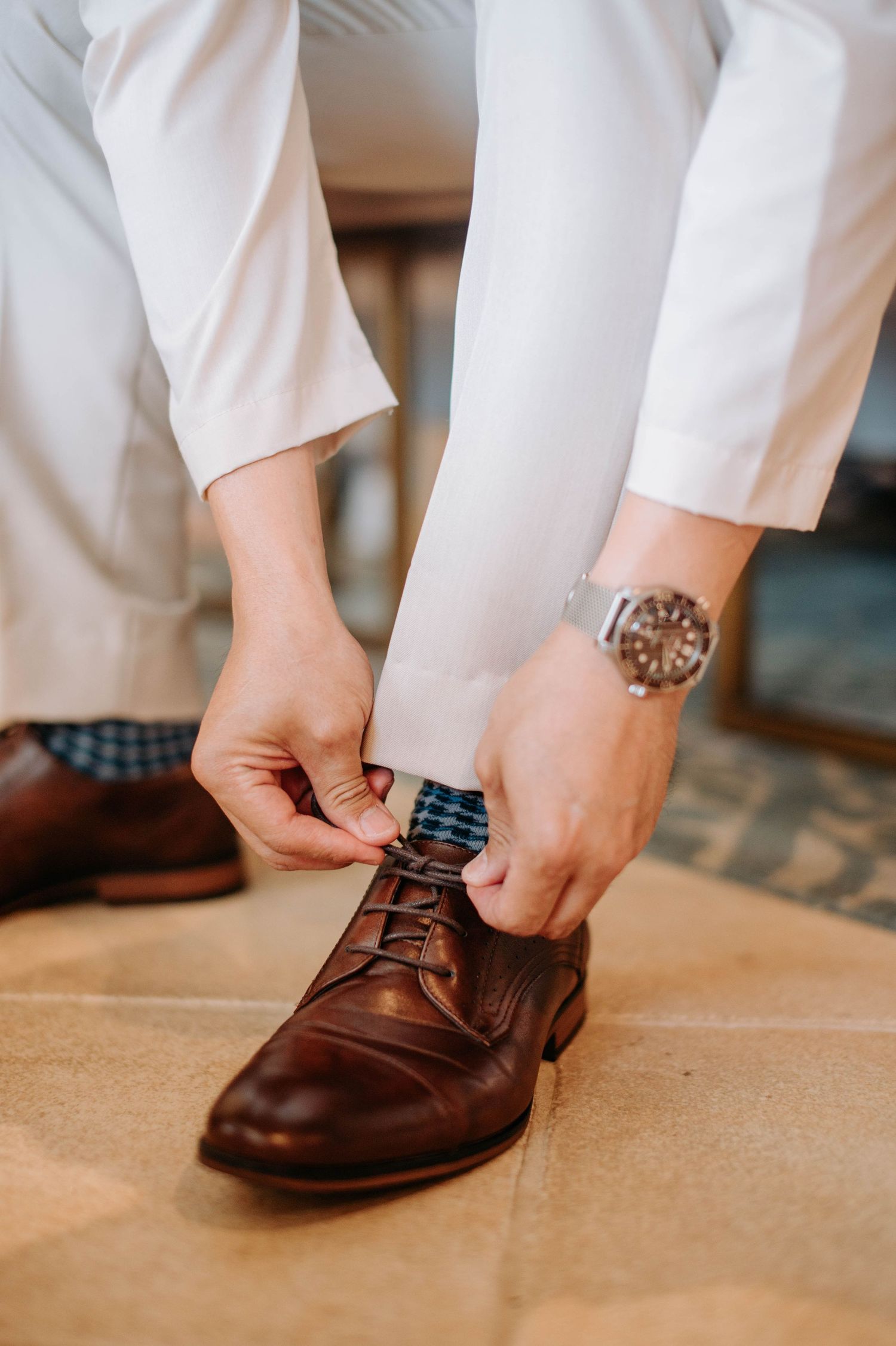 Close-up of hands tying brown leather dress shoes with elegant watch detail.