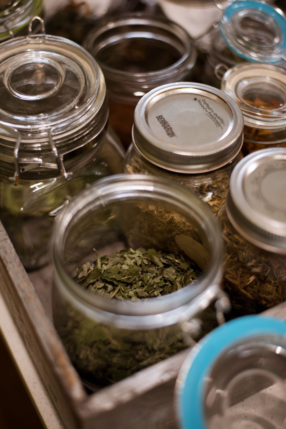 Glass jars containing dried herbs and spices arranged in a wooden tray.