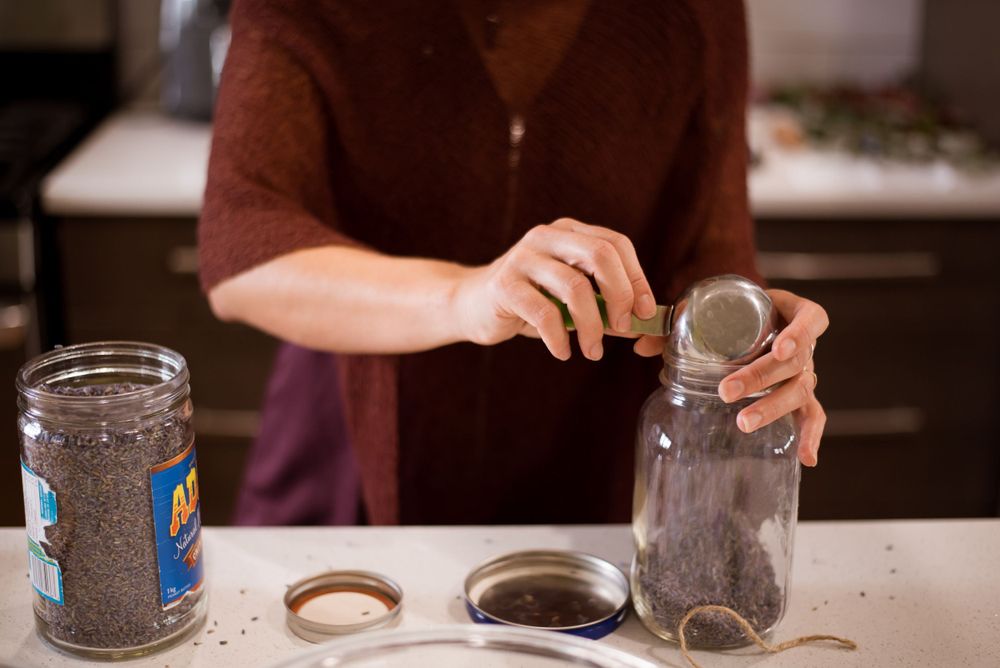 Hands working with glass jars and ingredients on a white counter surface.
