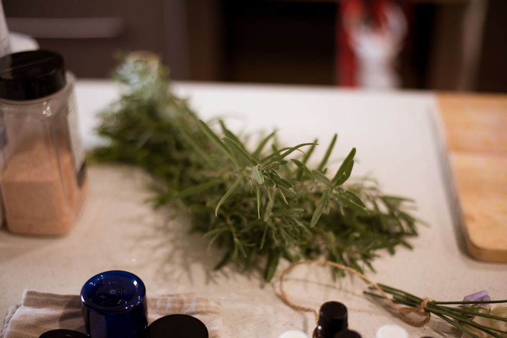 Fresh herbs and cooking ingredients laid out on white surface with glass containers.