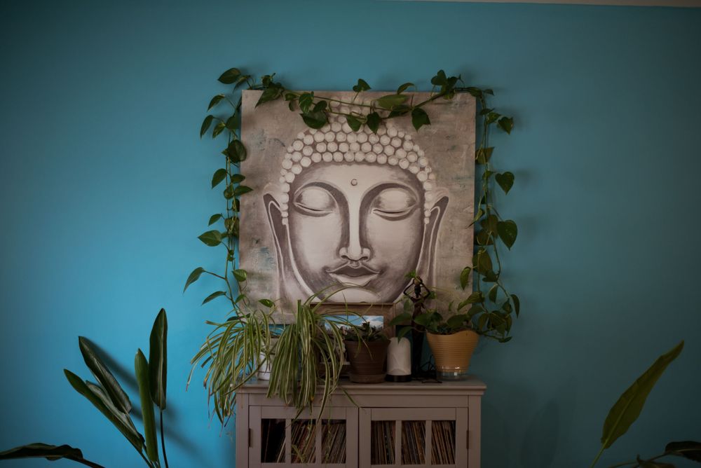 Buddha wall art with hanging plants against teal blue wall.