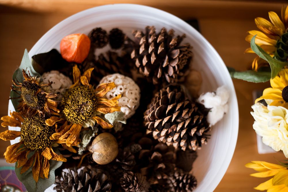 A decorative bowl filled with pine cones, dried flowers and sunflowers arranged in a rustic display.