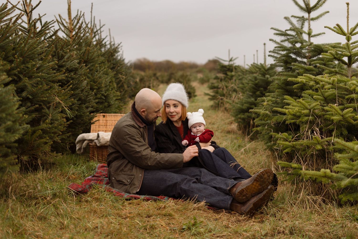 One Year old girl sitting on a red blanket for Christmas photos amongst christmas trees at The Christmas Tree Farm in Cowbridge.
