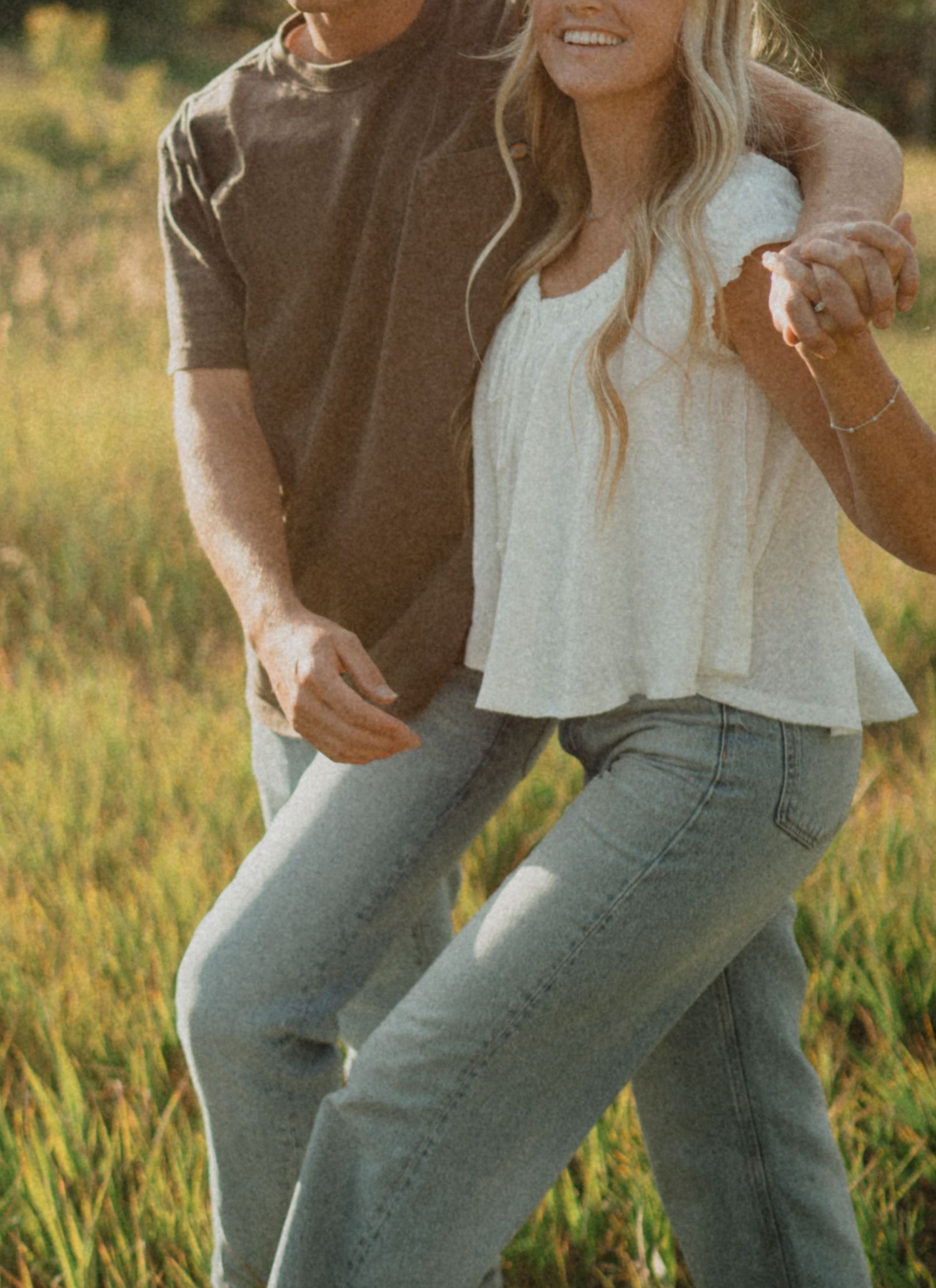 Couple in casual denim and white outfits photographed in a sunlit field.