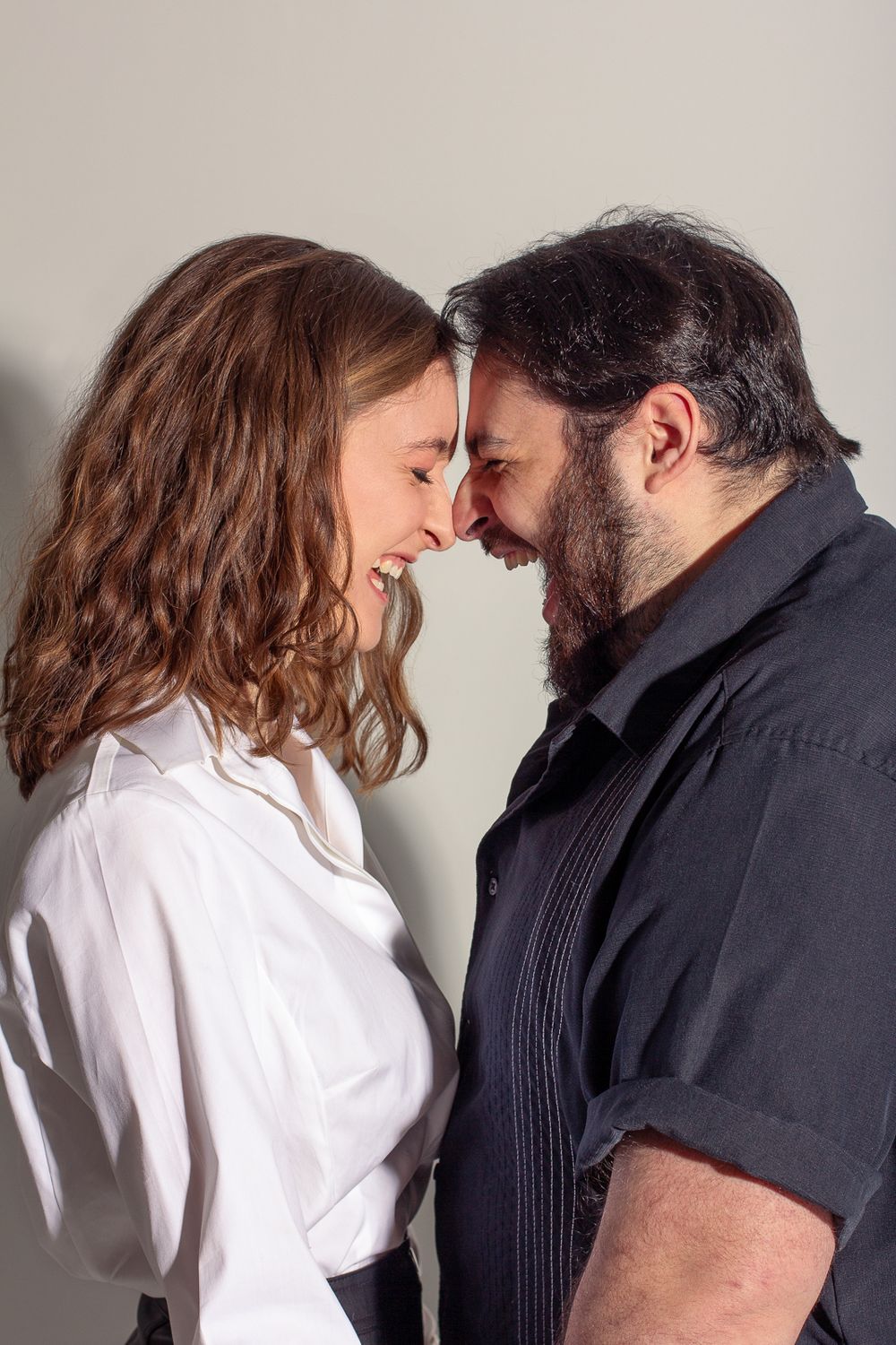 Intimate close-up portrait of a couple touching foreheads against a light background.