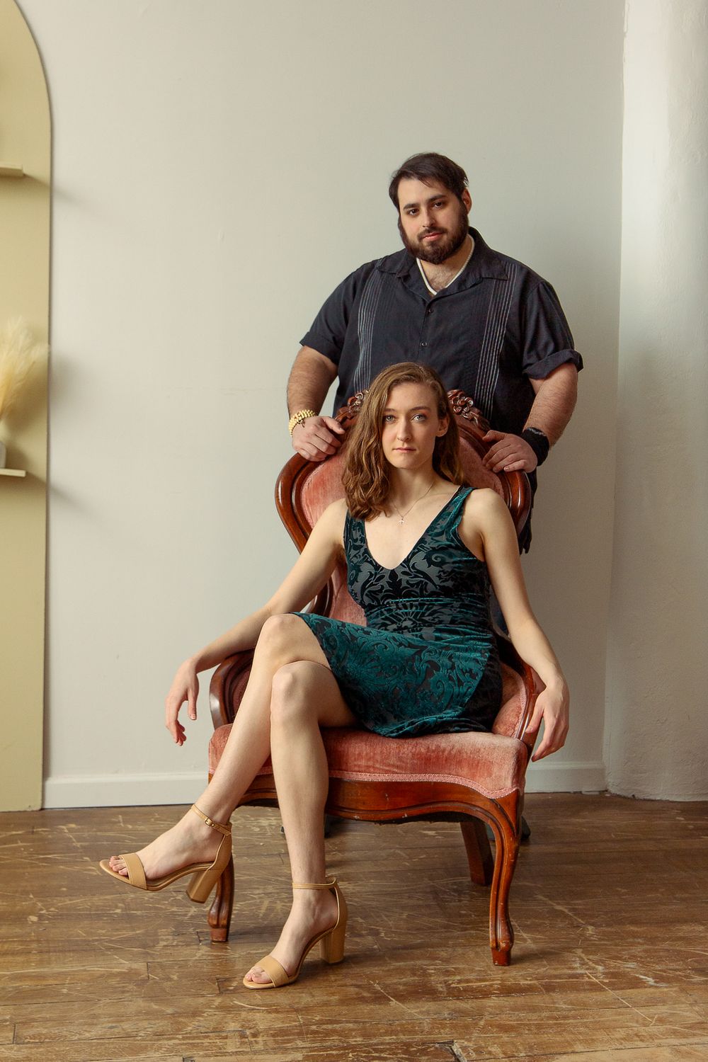 Studio portrait featuring two people posing with an antique chair against a minimalist backdrop.