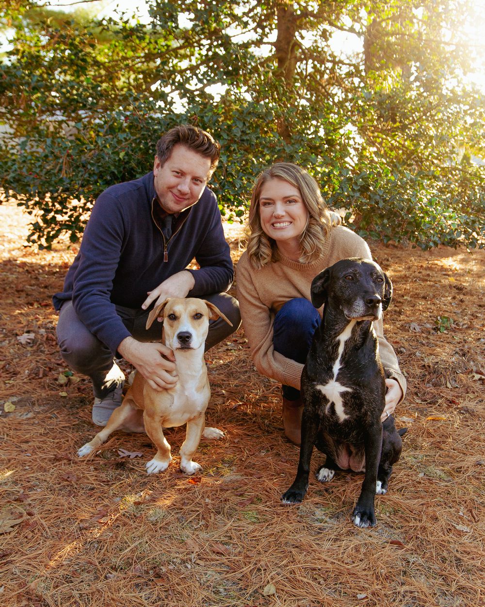 Two people and their dogs posing for photo outdoors during golden hour.