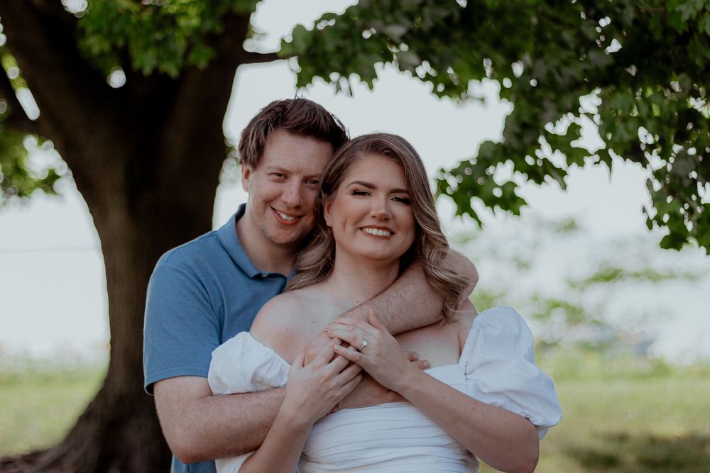 A romantic couple embraces outdoors under a tree during a photo session.