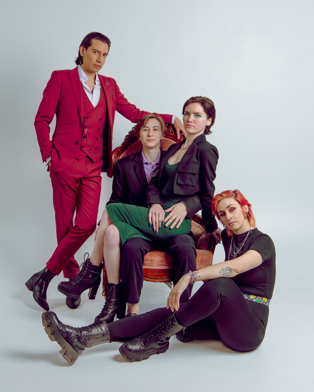 Four performers in coordinated outfits with red, purple and black tones pose stylishly against a studio backdrop.