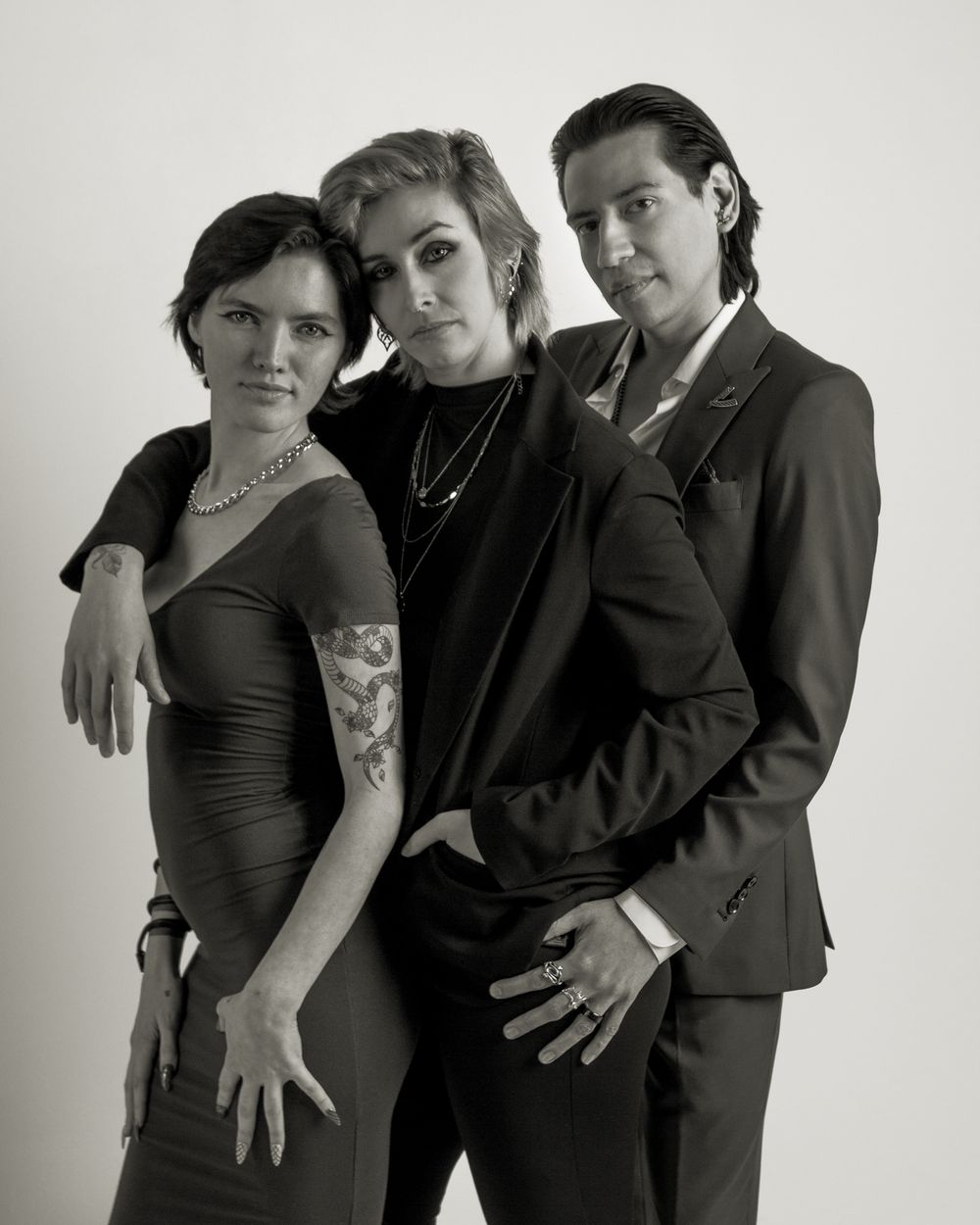 Three performers in formal black attire pose dramatically together for a moody black and white portrait.