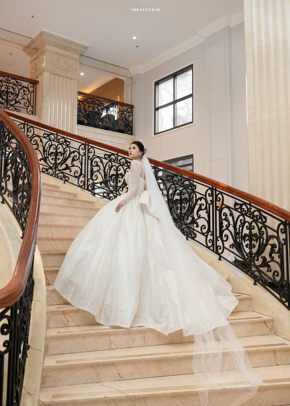 Bride in stunning ballgown poses on grand marble staircase with ornate railing.