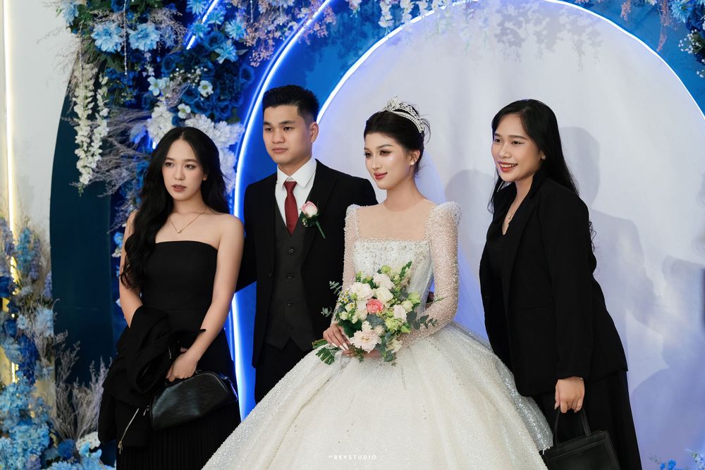 Wedding party poses in front of blue circular backdrop during reception celebration.