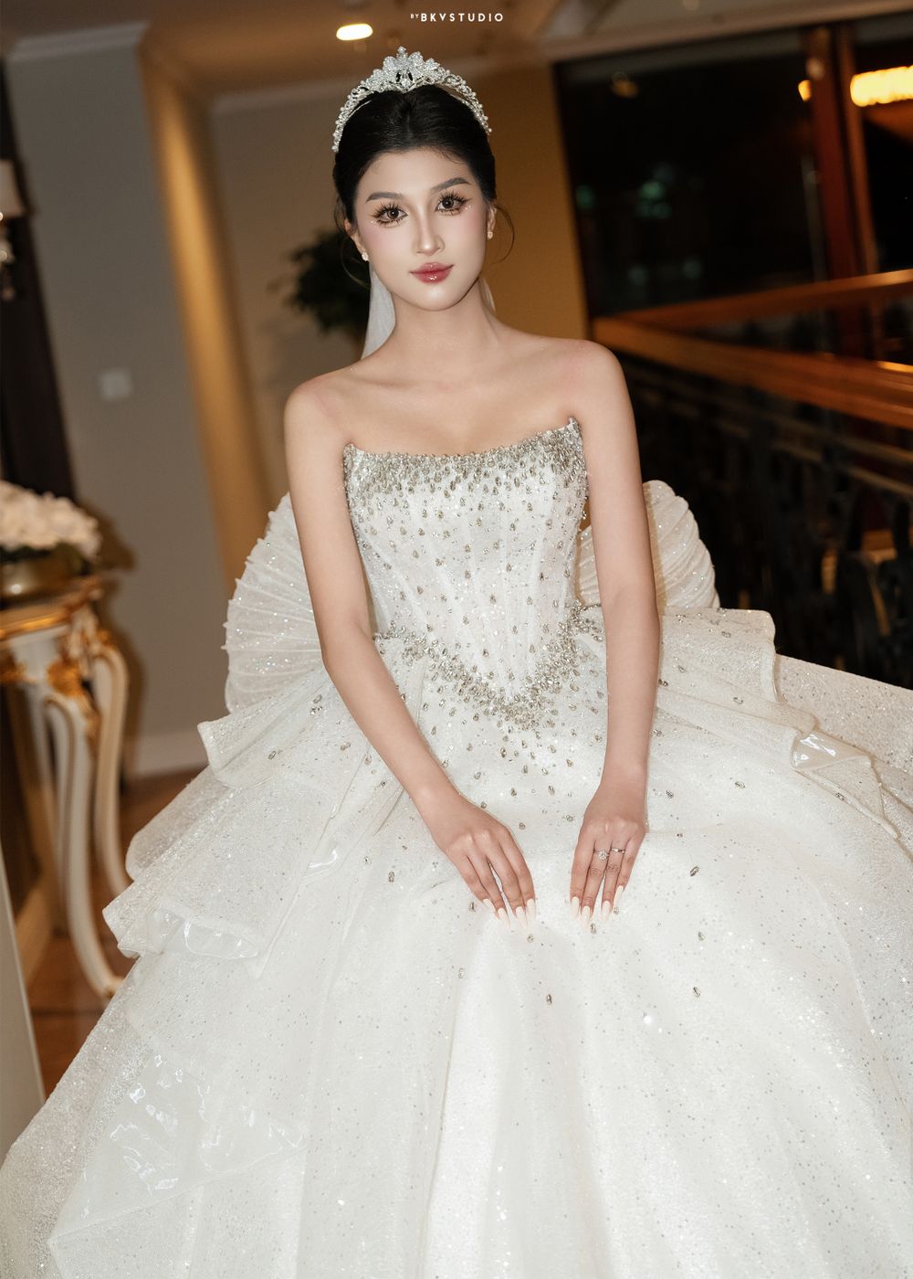 Bride wearing crystal-embellished strapless ballgown and tiara poses in elegant setting.