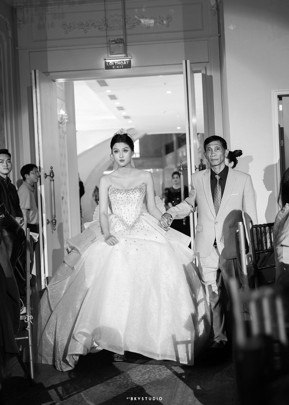 Black and white photo of newlyweds making grand entrance through elegant doorway.