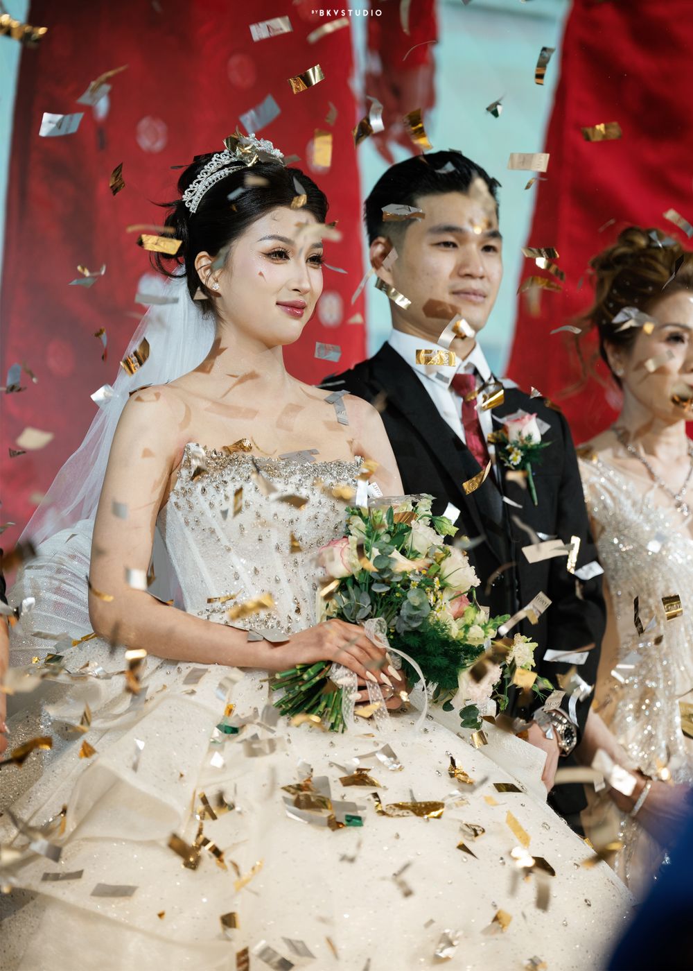 Celebratory moment with confetti falling on newlyweds against red backdrop.