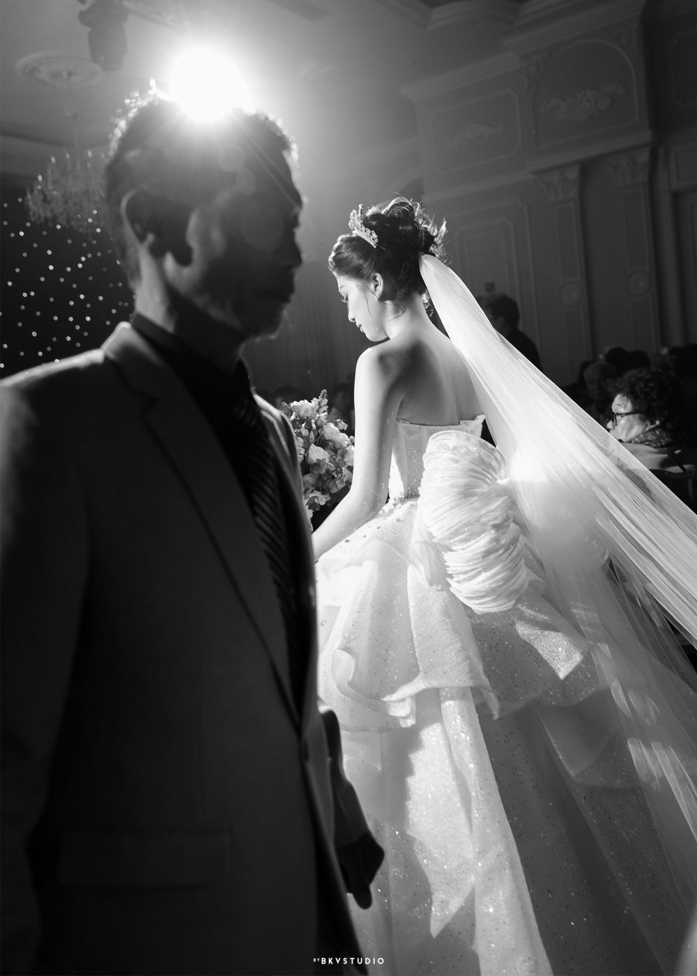 Dramatic black and white wedding photo capturing a couple in formal attire under spotlights.