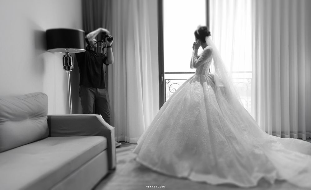Black and white photo of wedding preparation scene with flowing ballgown silhouette.