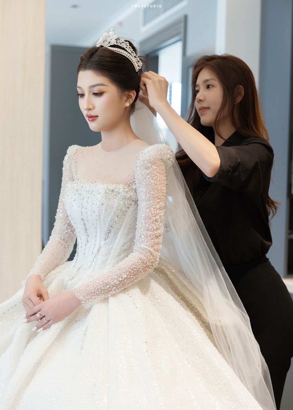Wedding preparation scene with stylist adjusting bridal crown and veil.