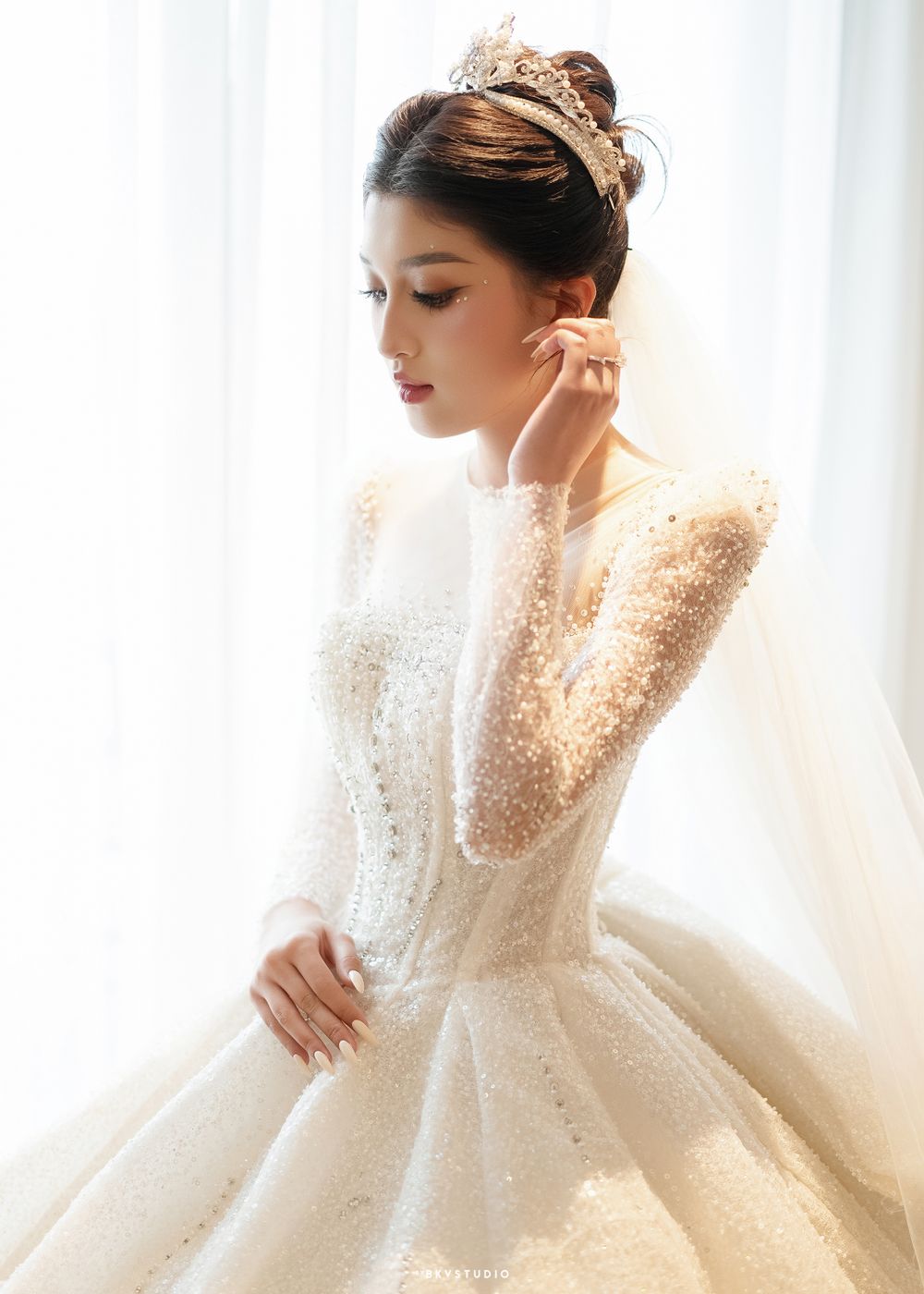 Side profile of bride in beaded long-sleeve wedding gown with sparkling crown.