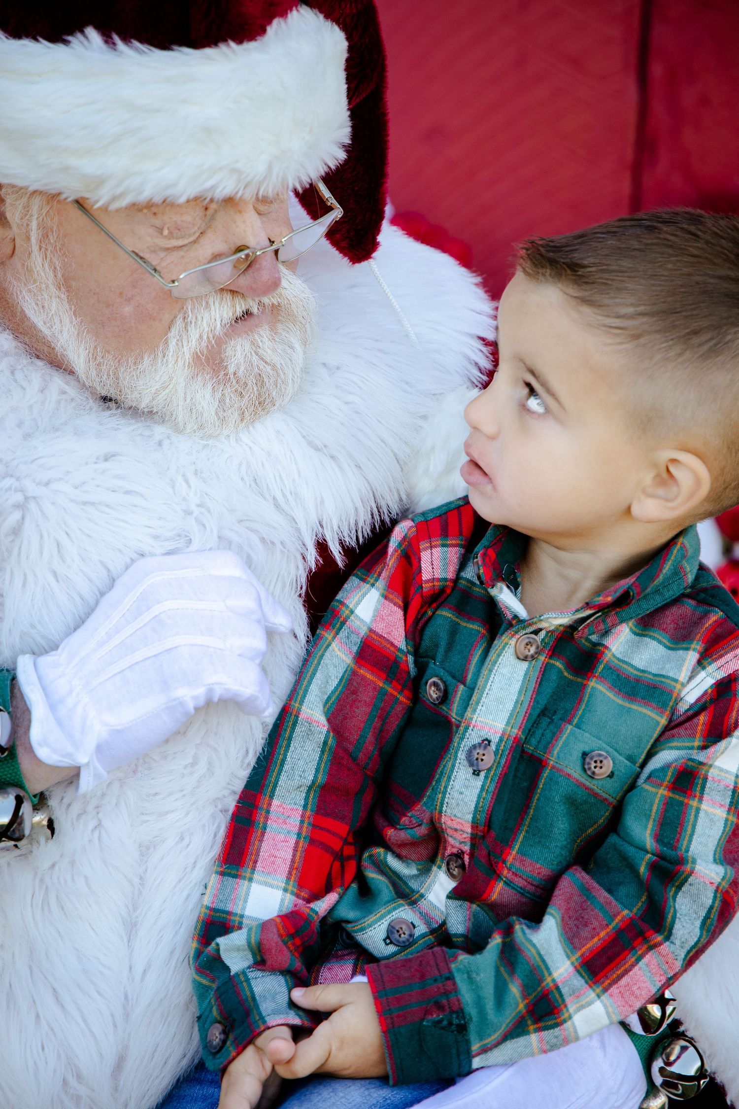 Child in plaid shirt meeting Santa Claus during holiday photo session.